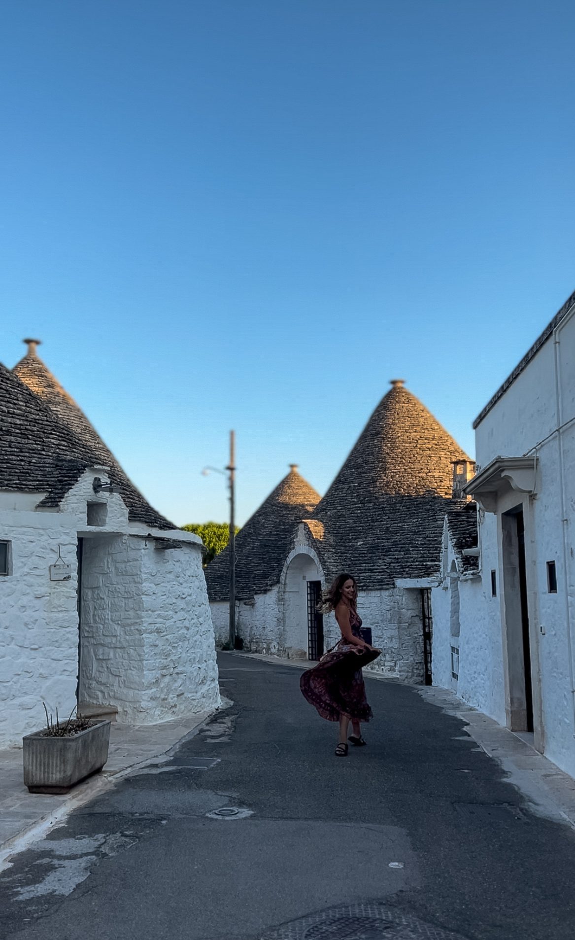 κορίτσι κάνει στροφή και φουσκώνει το φόρεμά της σε δρομάκι στο Αλμπερομπέλο, ανάμεσα στα παραδοσιακά πέτρινα σπιτάκια με την κωνική σκεπή.
