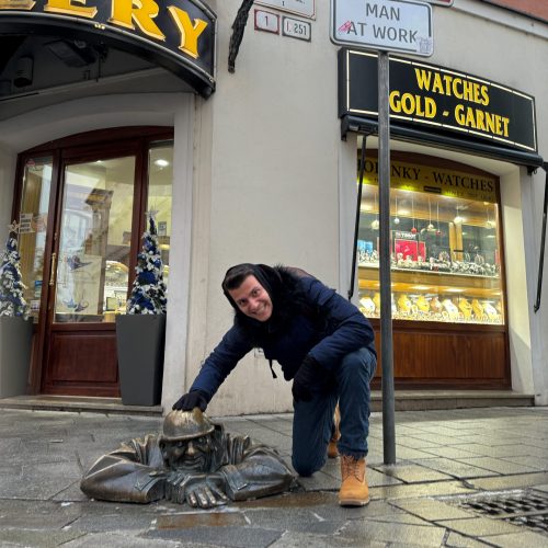 man-at-work-bratislava αγόρι έχει γονατίσει και χαιρετάει άγαλμα στο δρόμο που είναι μέσα σε φρεάτιο στην Μπρατισλάβα