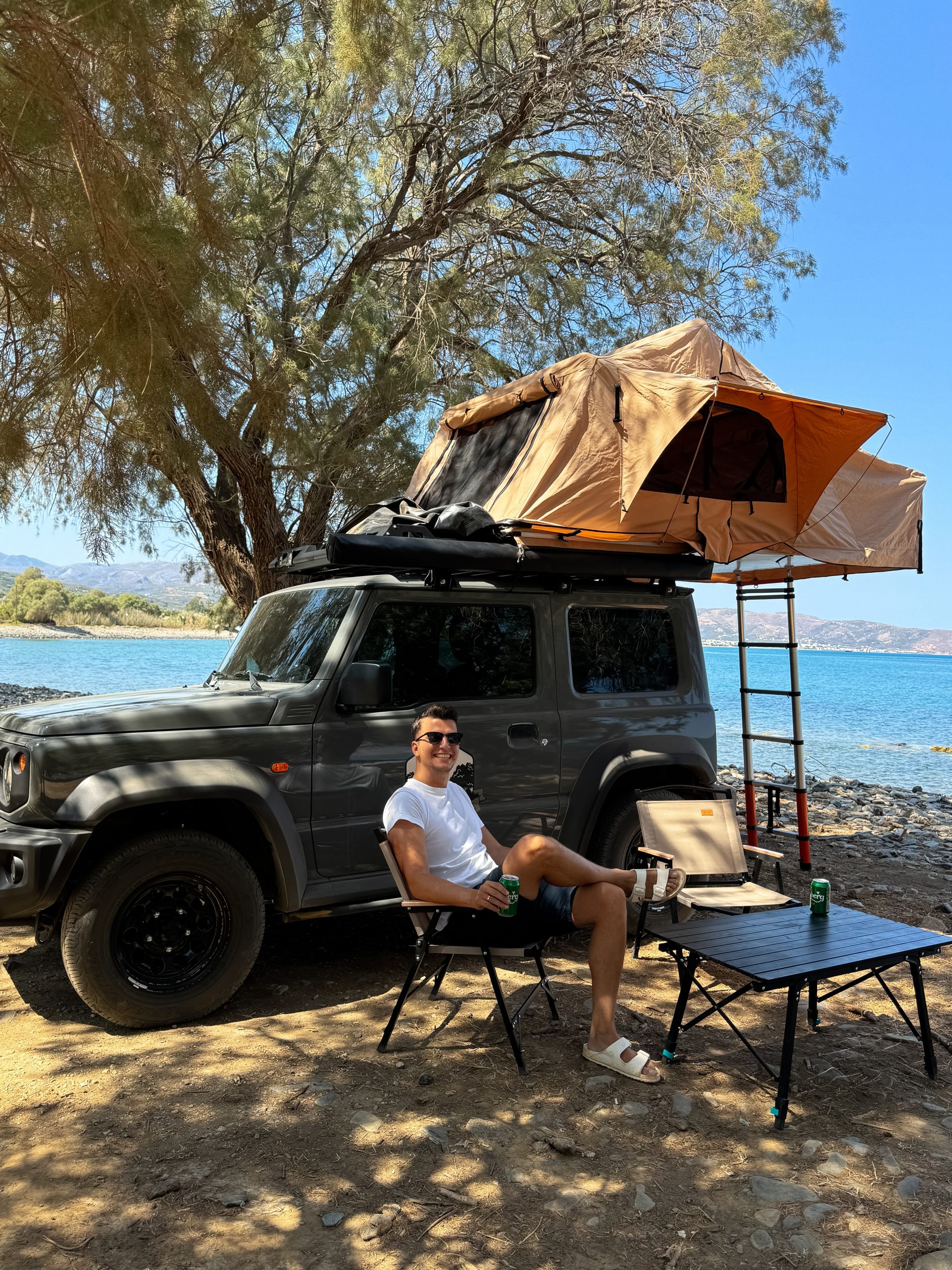 αγόρι κάνει camping με σκηνή πάνω σε αυτοκίνητο σε παραλία